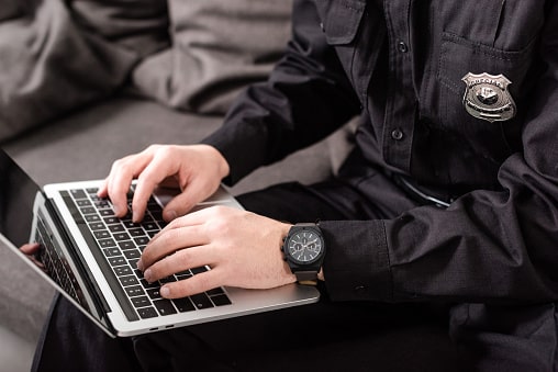 cropped view of policeman typing on laptop keyboard